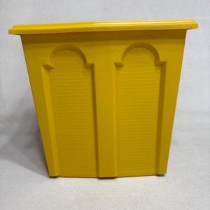May include: A bright yellow plastic wastebasket featuring a tapered rectangular shape. The exterior surface displays two recessed arch-shaped panels, each decorated with a subtle, repeating geometric grid pattern, topped by a wide, flat rim.