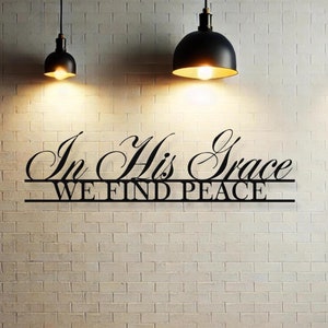 Puede incluir: Decoración de pared de metal negro con las palabras "In His Grace We Find Peace" en una pared de ladrillo blanco con tres lámparas colgantes.