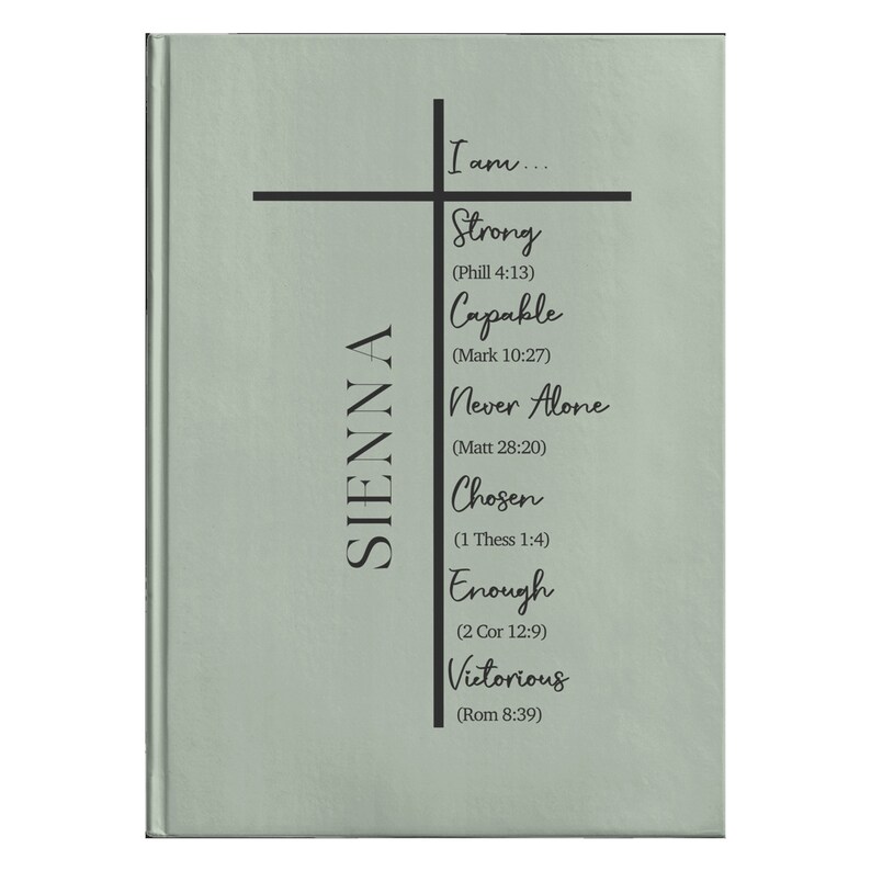 Op de afbeelding: Een saliegroen dagboek met een zwart kruis en de tekst "Ik ben... Sterk (Phill 4:13) Bekwaam (Markus 10:27) Nooit alleen (Matt 28:20) Uitverkoren (1 Thess 1:4) Genoeg (2 Kor 12:9) Overwinnaar (Rom 8:39)" en de naam "SIENNA" aan de linkerkant.