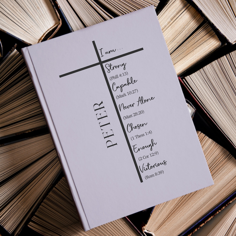 Op de afbeelding: Een lichtpaars boek met de naam "PETER" verticaal op de omslag gedrukt. Het boek heeft een zwart kruis met de woorden "Ik ben..." bovenaan. Het kruis heeft verschillende woorden en bijbelteksten erop gedrukt, waaronder "Sterk (Phill 4:13)", "Bekwaam (Mark 10:27)", "Nooit alleen (Matt 28:20)", "Uitverkoren (1 Thess 1:4)", "Genoeg (2 Cor 12:9)" en "Overwinnend (Rom 8:39)".