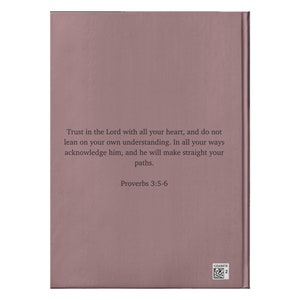Op de afbeelding: Een roze boek met de tekst "Trust in the Lord with all your heart, and do not lean on your own understanding. In all your ways acknowledge him, and he will make straight your paths. Proverbs 3:5-6" gedrukt op de omslag.