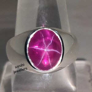 Peut inclure: Une bague en argent avec une pierre précieuse en rubis étoilé rose. La bague est sertie dans une bande simple avec une finition lisse. Le rubis est une coupe étoile, avec une étoile à six branches visible au centre de la pierre.