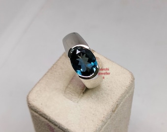 May include: A silver ring with a blue oval-shaped gemstone. The ring is set on a white display stand.