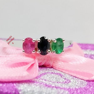 May include: A silver ring with three oval-shaped gemstones. The gemstones are red, black, and green.