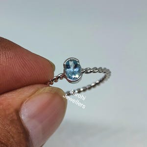 May include: A silver ring with a twisted band and a light blue oval gemstone. The ring is on a finger.