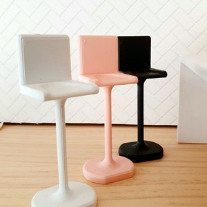 May include: Three miniature bar stools in white, pink and black. The stools are made of plastic and have a simple, modern design.