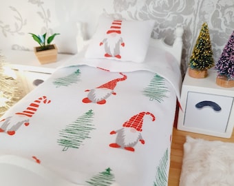 May include: A white doll bed with a red and green Christmas gnome themed bedding set. The bedding features a white background with green Christmas trees and red and white gnomes. The bed has a white headboard and footboard and is made of wood.