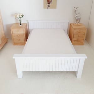 Può includere: Struttura letto in legno bianco con un materasso bianco e una testata bianca con doghe verticali. Due comodini in legno con cassetti sono su entrambi i lati del letto. Un quadro incorniciato di una girafe è appeso al muro sopra il letto.