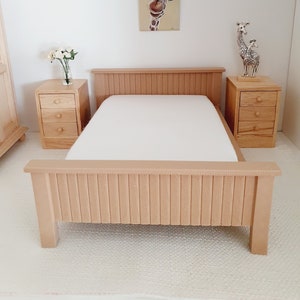 May include: A wooden dollhouse bed with a white mattress and a wooden headboard. The bed is in a dollhouse room with a giraffe painting on the wall and two wooden giraffe figurines on a bedside table.