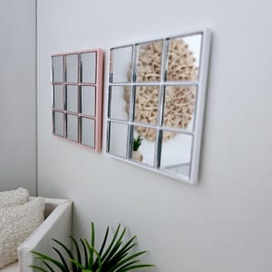 May include: Two square mirrors with a grid pattern of smaller mirrors. The mirror on the left has a pink frame and the mirror on the right has a white frame.