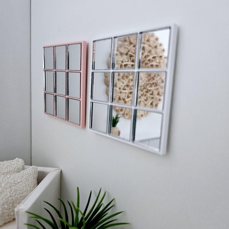 May include: Two square mirrors with a grid pattern of smaller mirrors. The mirror on the left has a pink frame and the mirror on the right has a white frame.