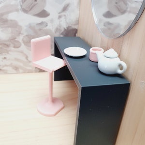 May include: A black vanity table with a pink chair, a white plate, a pink container, and a white teapot with a handle.