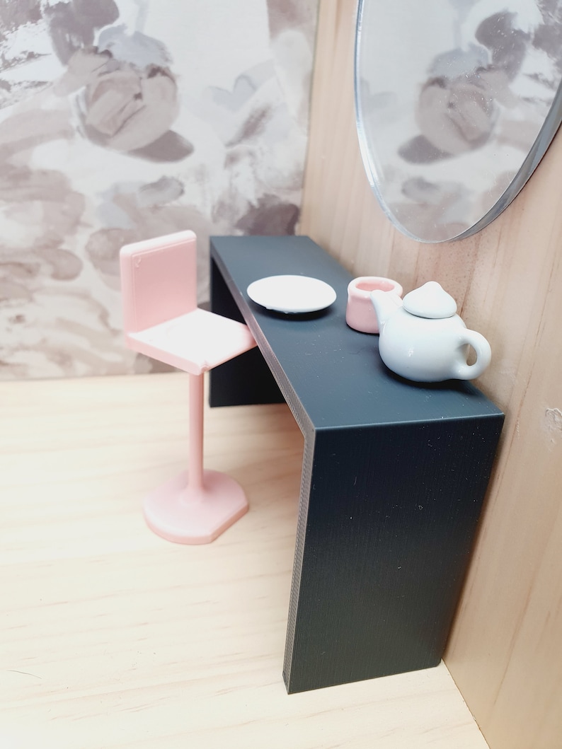 May include: A black vanity table with a pink chair, a white plate, a pink container, and a white teapot with a handle.