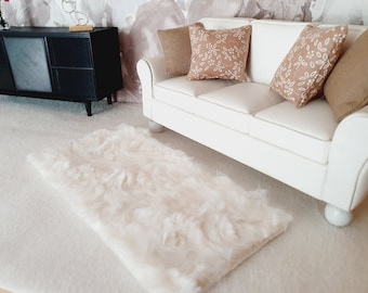 May include: A white faux fur rug with a white sofa and brown patterned throw cushions in the background.