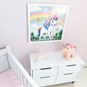 Pode incluir: Uma c&oacute;moda branca com quatro gavetas, uma decora&ccedil;&atilde;o de madeira arco-&iacute;ris rosa e branca e um brinquedo de pel&uacute;cia rosa em forma de unic&oacute;rnio. Uma imagem emoldurada de um unic&oacute;rnio com um arco-&iacute;ris e borboletas pendura na parede atr&aacute;s da c&oacute;moda.