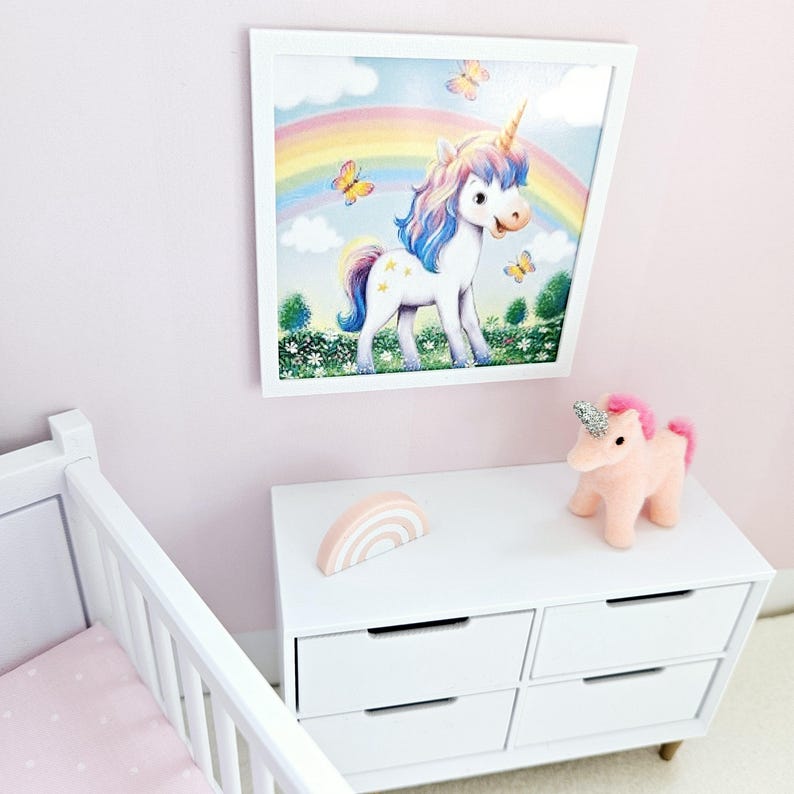 Pode incluir: Uma c&oacute;moda branca com quatro gavetas, uma decora&ccedil;&atilde;o de madeira arco-&iacute;ris rosa e branca e um brinquedo de pel&uacute;cia rosa em forma de unic&oacute;rnio. Uma imagem emoldurada de um unic&oacute;rnio com um arco-&iacute;ris e borboletas pendura na parede atr&aacute;s da c&oacute;moda.