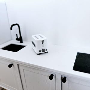 May include: White toaster on a white countertop with a black sink and faucet in the background.