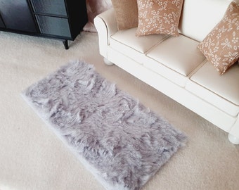 May include: A grey faux fur rug with a white background. The rug is rectangular and has a fluffy texture.