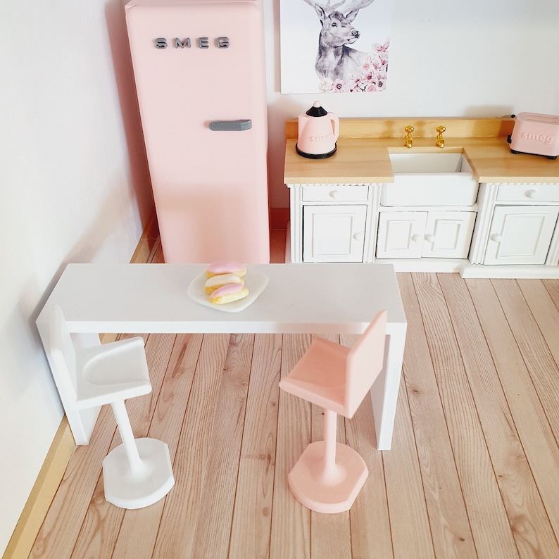 May include: A pink miniature kitchen set with a white countertop, two white bar stools, a pink refrigerator with the word "SMEG" on it, a white sink, and a white cabinet with two doors.