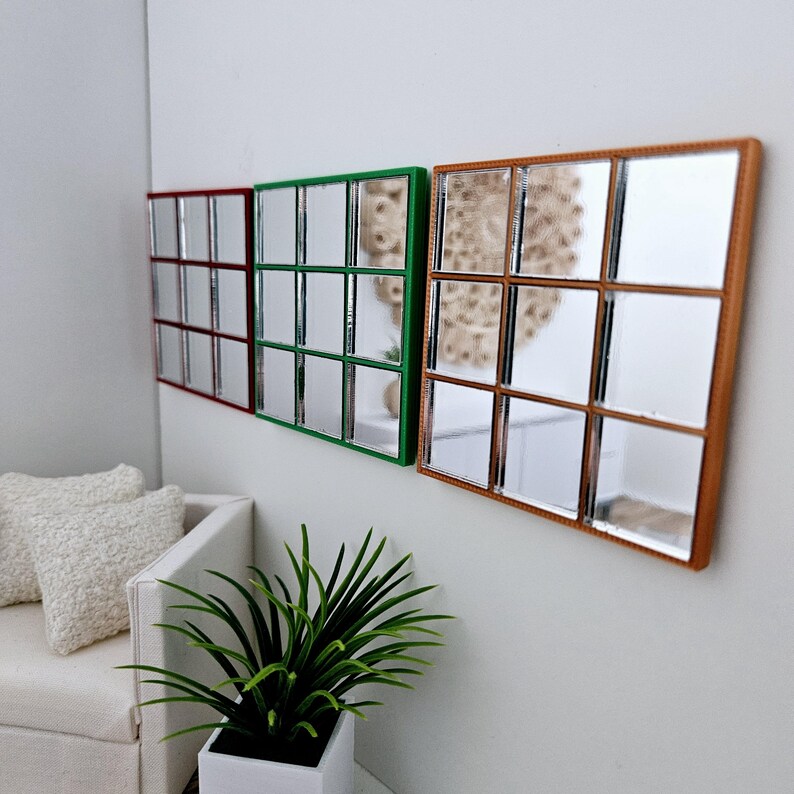 May include: Three square mirrors with a grid pattern, each with a different colored frame. The mirrors are hung on a white wall. The mirror on the left has a red frame, the middle mirror has a green frame, and the mirror on the right has a brown frame.