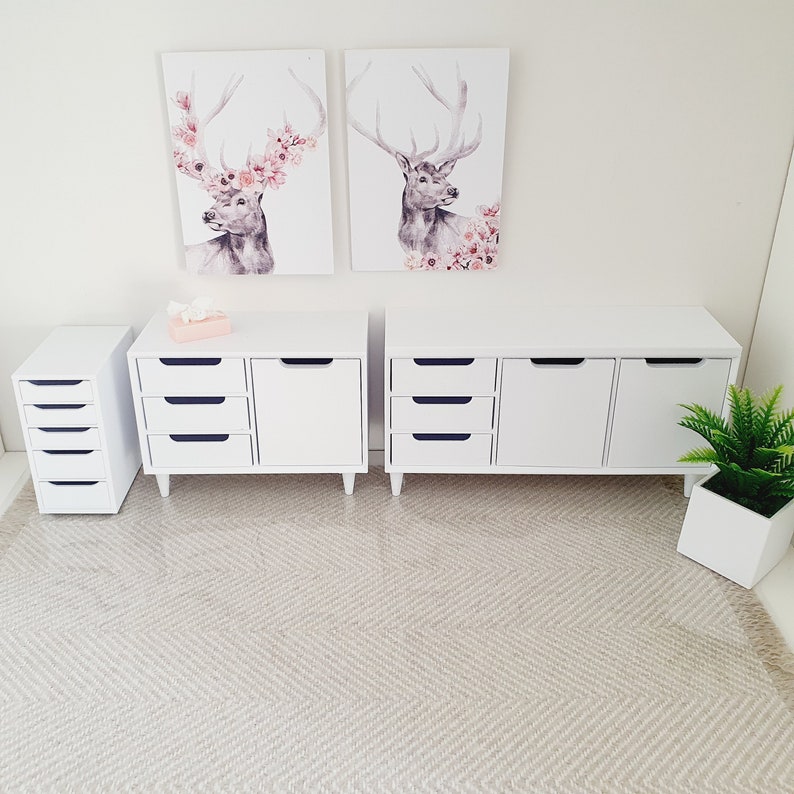 Puede incluir: Dos c&oacute;modas blancas con cajones y puertas, una c&oacute;moda blanca peque&ntilde;a con cajones y una alfombra blanca con un patr&oacute;n de espiga. Dos impresiones enmarcadas de ciervos con acentos florales cuelgan en la pared sobre las c&oacute;modas.