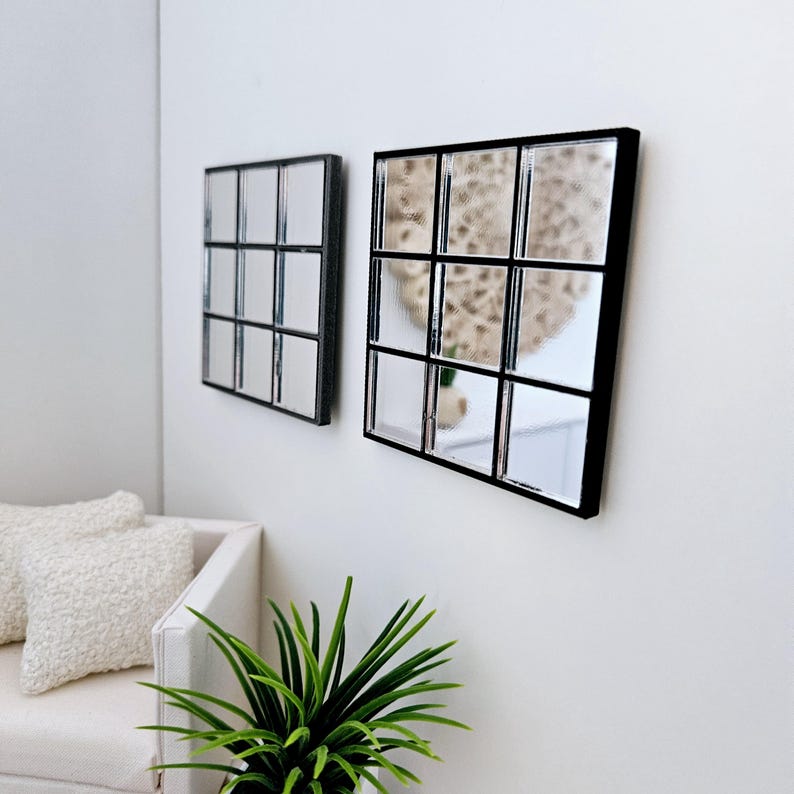 May include: Two square mirrors with black frames, each divided into nine smaller squares. The mirrors are hanging on a white wall.