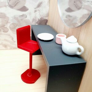 May include: A red bar stool with a black table top. There is a white plate, a pink cup, and a white teapot on the table.