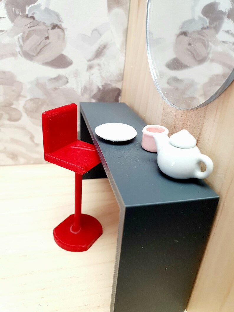May include: A red bar stool with a black table top. There is a white plate, a pink cup, and a white teapot on the table.