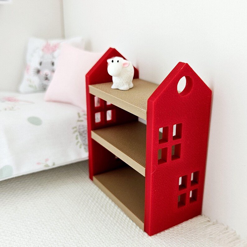 May include: A red wooden shelf unit with two shelves and a white lamb figurine on the top shelf. The shelf unit has a house-shaped design with cut-out windows.