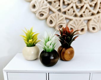 May include: Three miniature potted plants with different coloured leaves and wooden pots. The plants are in a white planter with three drawers.