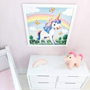 Pode incluir: Uma imagem emoldurada branca de um unic&oacute;rnio em p&eacute; em um campo com um arco-&iacute;ris ao fundo. O unic&oacute;rnio tem uma crina e uma cauda azuis e rosas. H&aacute; borboletas voando ao redor do unic&oacute;rnio. A imagem est&aacute; pendurada em uma parede rosa acima de uma c&ocirc;moda branca com uma decora&ccedil;&atilde;o em forma de arco-&iacute;ris rosa no topo.