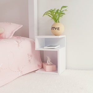 May include: White bedside table with two shelves. The top shelf has a small potted plant with the word "LOVE" on the pot. The bottom shelf has a tissue box and a small white rectangle.