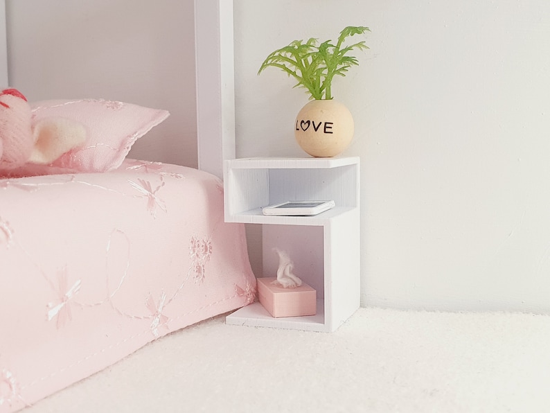 May include: White bedside table with two shelves. The top shelf has a small potted plant with the word "LOVE" on the pot. The bottom shelf has a tissue box and a small white rectangle.