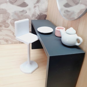 May include: A white bar stool with a black table and a white plate, a pink ceramic container, and a white teapot with a lid.