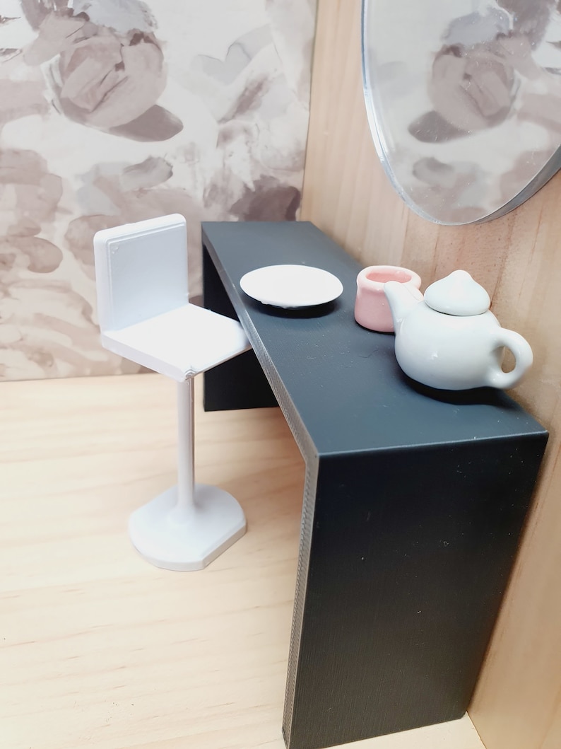 May include: A white bar stool with a black table and a white plate, a pink ceramic container, and a white teapot with a lid.