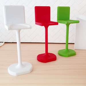 May include: Three bar stools in different colours: white, red, and green. The stools have a simple, modern design with a square seat and a single, curved leg.