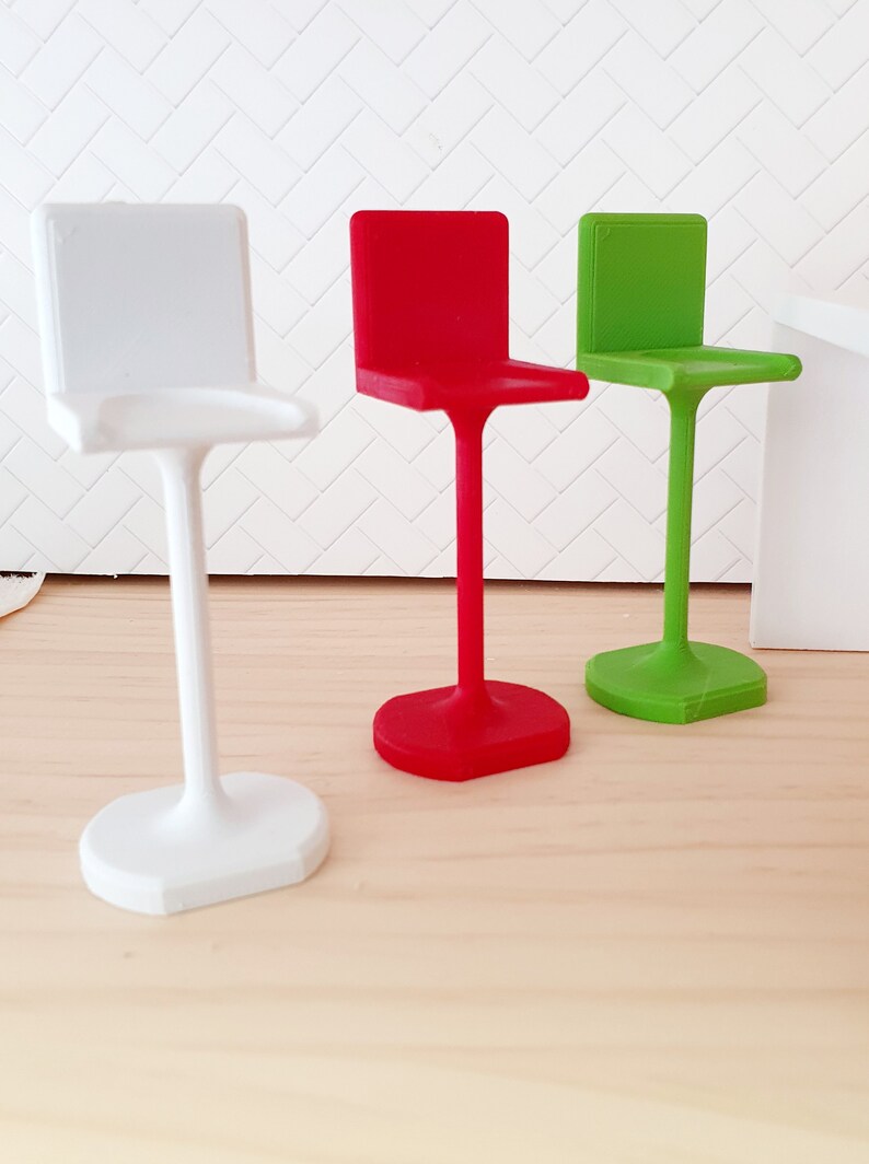 May include: Three bar stools in different colours: white, red, and green. The stools have a simple, modern design with a square seat and a single, curved leg.