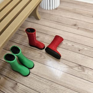 Könnte beinhalten: Miniatur-Gummistiefel in Rot und Grün mit schwarzen Sohlen liegen auf einer Holzoberfläche. Zwei rote und zwei grüne Stiefel sind zu sehen. Die kleinen Stiefel sind wahrscheinlich für Puppen oder Dekorationszwecke gedacht.
