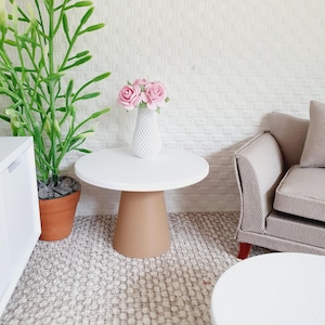 Puede incluir: Una mesa auxiliar redonda blanca con una base de pedestal marrón. Un jarrón blanco con flores rosas se encuentra sobre la mesa.