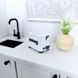 May include: White Smeg toaster with black accents on a white countertop. The toaster has two slots and a lever on the side.