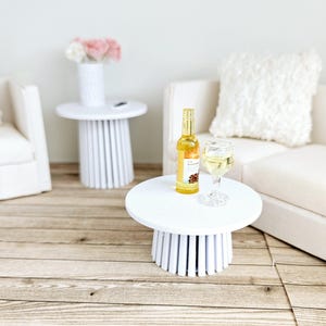 May include: Two white side tables with a white sofa and a bottle of wine and a glass of wine on one of the tables.