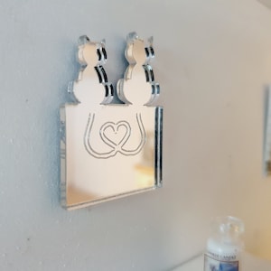 May include: A silver mirror with a heart design and two cats on top. The mirror is rectangular and has a beveled edge.
