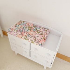 May include: White chest of drawers with four drawers and a floral patterned changing mat on top.