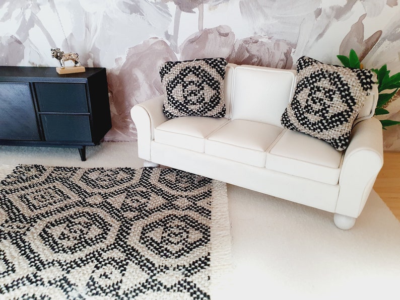 May include: Miniature living room set with a white sofa, two patterned pillows, and a black and white rug. A black cabinet and decorative items complete the scene. The rug has a geometric design.