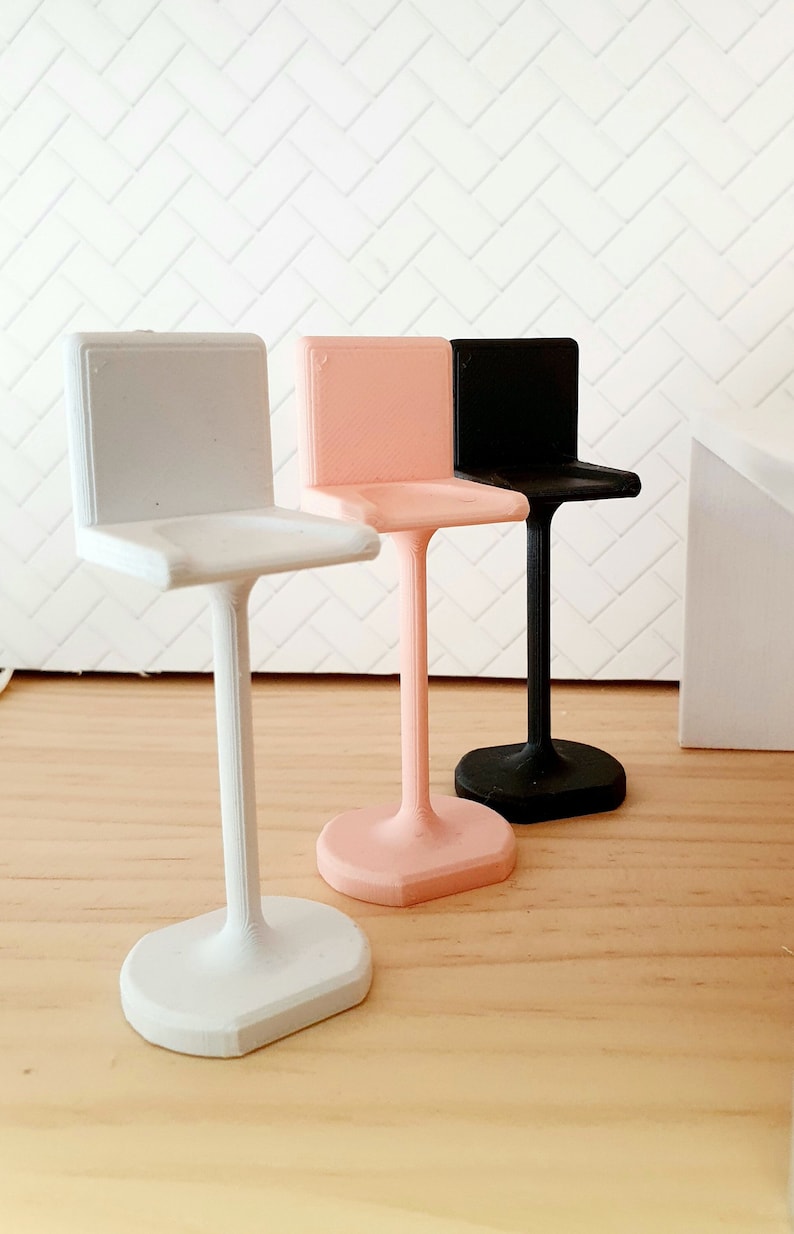 May include: Three miniature bar stools in white, pink and black. The stools are made of plastic and have a simple, modern design.
