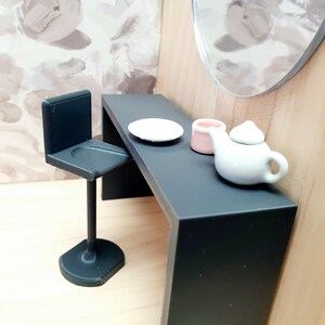 May include: A black vanity table with a white plate, a pink container, and a white teapot. A black stool sits next to the table.