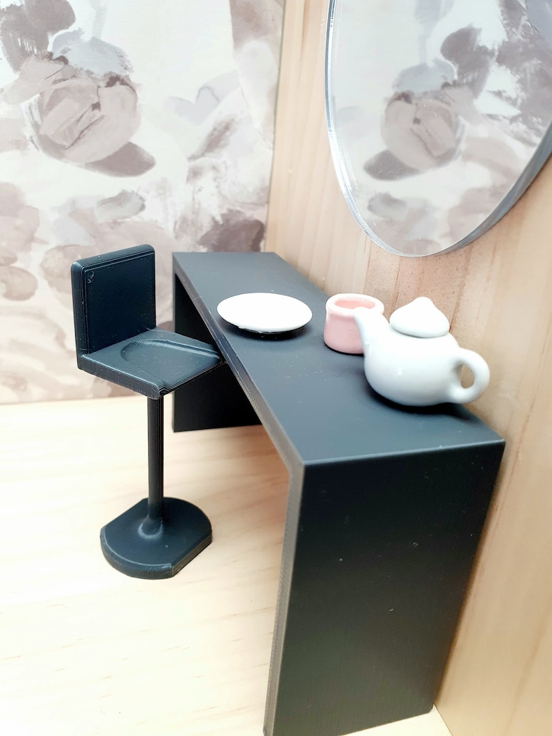 May include: A black vanity table with a white plate, a pink container, and a white teapot. A black stool sits next to the table.
