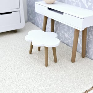 May include: A white cloud-shaped side table with wooden legs sits on a white shag rug in front of a white desk with a drawer and wooden legs.