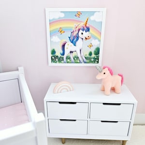 Pode incluir: Uma c&oacute;moda branca com seis gavetas, um brinquedo de peluche de unic&oacute;rnio rosa e uma decora&ccedil;&atilde;o de arco-&iacute;ris de madeira colorida. Uma imagem emoldurada de um unic&oacute;rnio de p&eacute; num campo com um arco-&iacute;ris acima dele pendura na parede atr&aacute;s da c&oacute;moda.