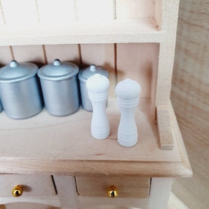May include: Two white wooden salt and pepper shakers on a wooden shelf with silver canisters in the background.